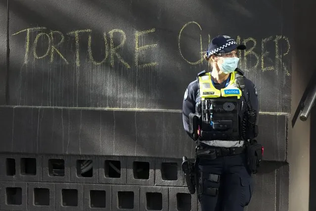 A police officer stands by a slogan on the wall outside the Park Hotel, used as an immigration detention hotel where tennis player Novak Djokovic is confined in Melbourne, Australia, Sunday, January 9, 2022. After five nights in hotel detention Djokovic will get his day in court on Monday, Jan. 10, in a controversial immigration case that has polarized opinions in the tennis world and elicited heartfelt support for the star back home in his native Serbia. (Photo by Mark Baker/AP Photo)