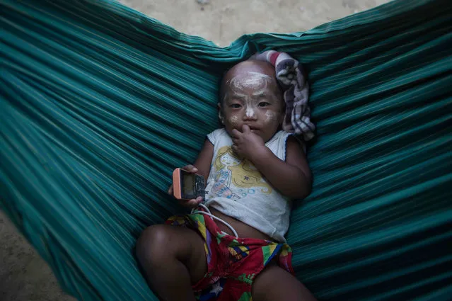 This photo taken on March 8, 2018 shows a Rakhine baby lying in a cradle in Koe Tan Kauk village, Rathedaung township in Myanmar' s Rakhine State. Buddhist flags hang limply from bamboo poles at the entrance to Koe Tan Kauk, a “model” village for ethnic Rakhine migrants shuttled north to repopulate an area once dominated by Rohingya Muslims. (Photo by Phyo Hein Kyaw/AFP Photo)