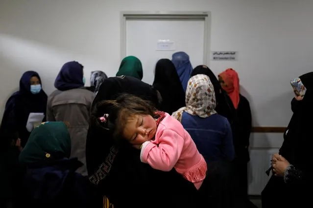 A mother holds her child as she rests in her arms, while women line up outside of a doctor's room, at a hospital in Bamiyan, Afghanistan on March 2, 2023. (Photo by Ali Khara/Reuters)