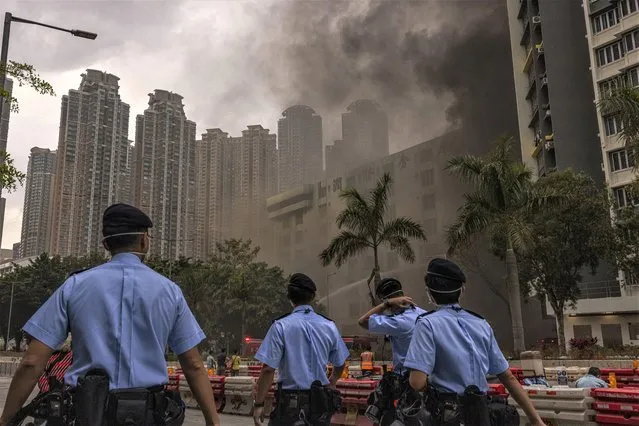 Police officers patrol as a warehouse burns in Cheung Sha Wan in Hong Kong, Friday, March 24, 2023. Hong Kong firefighters were battling a blaze Friday at a warehouse that forced 3,400 people to evacuate, including students, police said.  (Photo by Louise Delmotte/AP Photo)