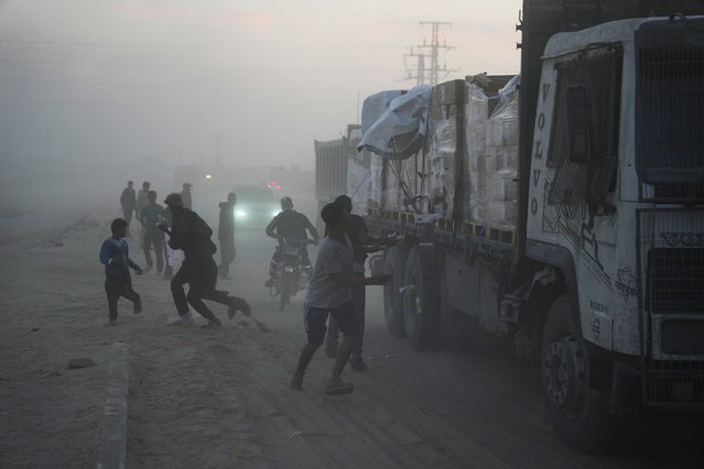 Palestinians rush toward trucks carrying aid from the World Food Programme (WFP) as they drive through Deir al-Balah in central Gaza, Saturday, November 8, 2025. (Photo by Abdel Kareem Hana/AP Photo)