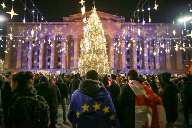 Demonstrators with an EU and a Georgian, Ukrainian national flags attend an anti-government rally outside the Parliament building decorated for Christmas and the New Year festivities, in Tbilisi, Georgia, Sunday, December 22, 2024. (Photo by Zurab Tsertsvadze/AP Photo)