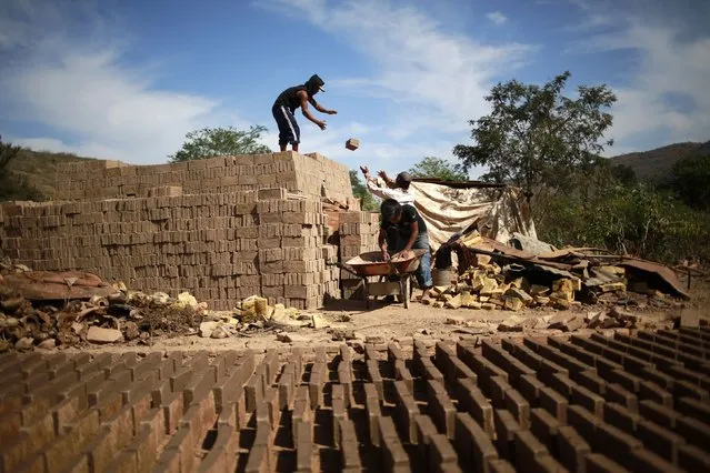 A worker standing on a pile of bricks receives bricks from another worker at a brick factory in Tixtla, on the outskirts of Chilpancingo, in the Guerrero state, January 26, 2015. (Photo by Jorge Dan Lopez/Reuters)