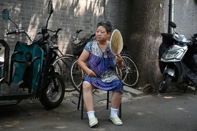 A woman fans herself while resting in the shade in an alley during a heatwave in Beijing on June 23, 2023. China issued its highest-level heat alert for northern parts of the country on June 23 as the capital baked in temperatures hovering around 40 degrees Celsius (104 Fahrenheit). (Photo by Greg Baker/AFP Photo)