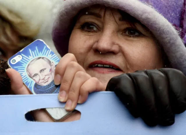 A woman holds a smartphone bearing an image of Russian President Vladimir Putin as Pro-Kremlin supporters march in central Moscow on November 4, 2016 as they celebrate the National Unity Day, marking the 404th anniversary of the 1612 expulsion of Polish occupation forces from the Kremlin. The statue commemorates Russian Prince Dmitry Pozharsky and merchant Kuzma Minin, who gathered a volunteer army and expelled the forces of the Polish-Lithuanian Commonwealth under the command of King Sigismund III of Poland from Moscow in 1612. (Photo by Vasily Maximov/AFP Photo)