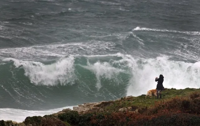 A woman takes a photograph of crashing waves on Brittany's Atlantic coast near Esquibien, in western France, January 1, 2016. (Photo by Mal Langsdon/Reuters)