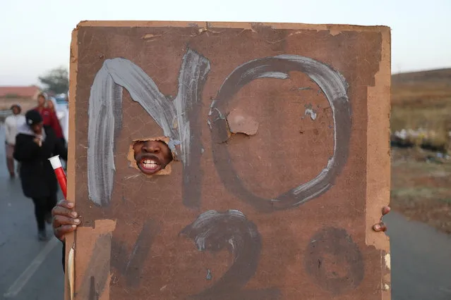 A member of the Lenasia community shouts through a hole in her poster during a protest against the recent land invaders who tried to settle on an open piece of land near their houses, in Johannesburg, South Africa, 05 September 2018. The area has seen thousands of illegal shacks being erected over the past months as both South African and foreign nationals moved to the city to live. The issues of land, and its redistribution, is an important topic in South Africa as the government looks at the option of handing land to previously disadvantaged communities without payment to the land owners. Houses in Lensasia south, where these invasions happened, have lost 40 percent value as residents tried to stop trespassers from taking more land. (Photo by Kim Ludbrook/EPA/EFE)