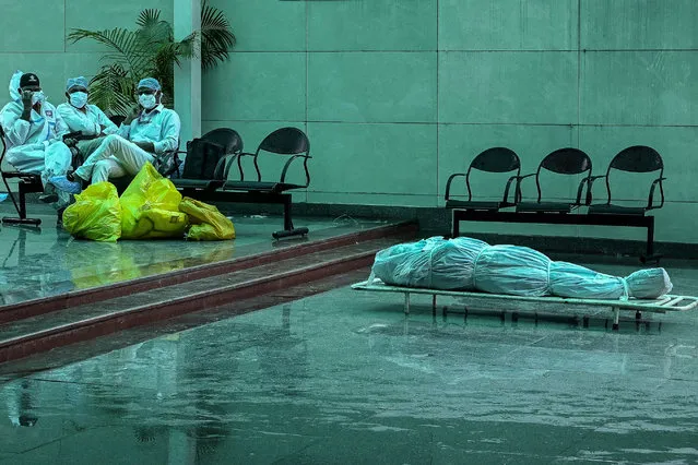 Health workers wearing Personal Protective Equipment (PPE) suits sit next to the dead body of a person who died due to the Covid-19 coronavirus, at a crematorium in New Delhi on May 19, 2021. (Photo by Prakash Singh/AFP Photo)