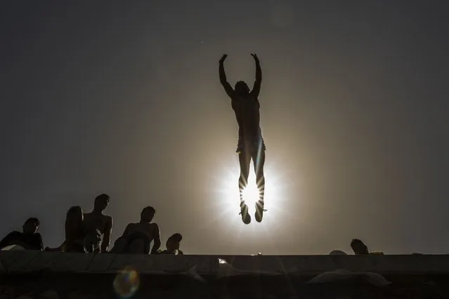 A youth jumps into the Mediterranean Sea off the corniche during a lockdown over Orthodox Easter to curb the spread of coronavirus in Saida, Lebanon, Sunday, May 2, 2021. The lockdown and curfew began early Saturday and lasts into Tuesday morning. (Photo by Hassan Ammar/AP Photo)