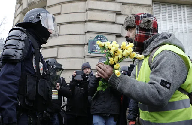 A demonstrator wearing his yellow vest holds a bouquet of roses in front of a riot police officer during a protest Saturday, December 15, 2018 in Paris. (Photo by Kamil Zihnioglu/AP Photo)