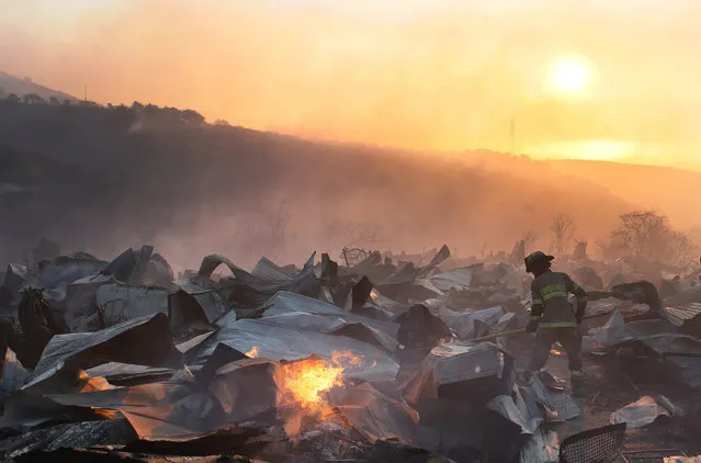 A firefighter removes the remains of a burned house on a hill, where more than 100 homes were burned due to forest fire but there have been no reports of death, local authorities said in Valparaiso, Chile January 2, 2017. (Photo by Rodrigo Garrido/Reuters)