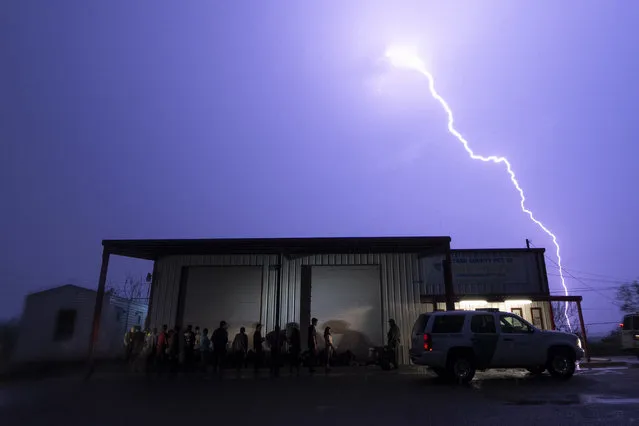 A lightning bolt is seen in the sky during a storm as migrants are lined up as they are processed by immigration officials outside the Starr County precinct 2 building after they crossed the Texas-Mexico border early Saturday, May 13, 2023, in Fronton, Texas. (Photo by Julio Cortez/AP Photo)