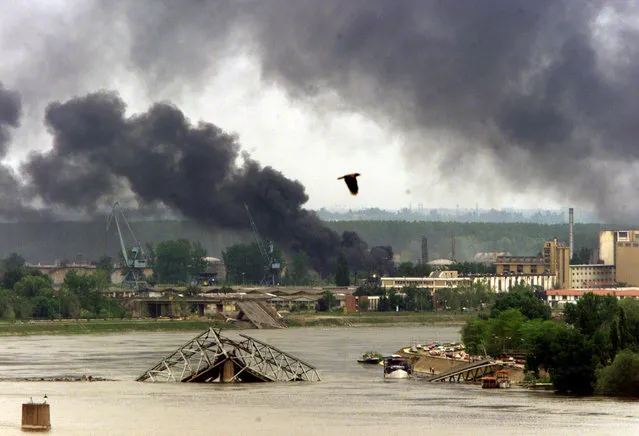 Smoke rises over the Danube river in the northern Serbian town of Novi Sad while an oil refinery burns after being repeatedly targeted by NATO air raids, May 1999. (Photo by Desmond Boylan/Reuters)