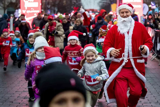Children dressed in Santa Claus hats run from the start line of the traditional Christmas run along the streets of Vilnius, Lithuania, Saturday, December 9, 2023. The festive run attracts many hundreds of people to the capital dressed as Santa Claus to take part in the sporting event. (Photo by Mindaugas Kulbis/AP Photo)