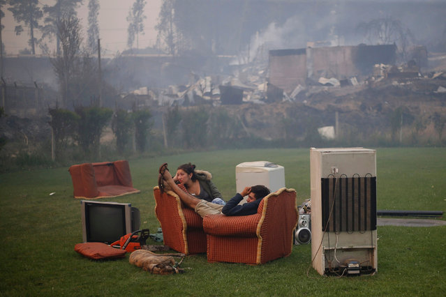 A young couple rest in a football field after a forest fire devastated Santa Olga, 240 kilometres south of Santiago, on January 26, 2017. Six people – among them four firefighters and two police – have now been killed battling vast forest fires in central Chile, officials said Wednesday. Multiple blazes have ravaged 238,000 hectares (588,000 acres) and are growing, the National Forestry Corporation said in a statement. (Photo by Pablo Vera Lisperguer/AFP Photo)