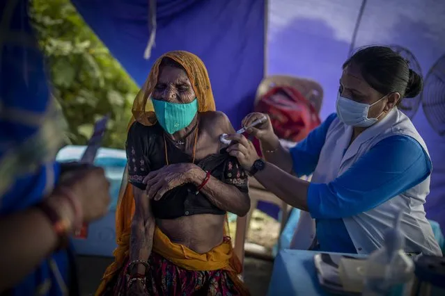 An elderly woman reacts as a health worker inoculates her during a special vaccination drive for homeless and migrant workers against COVID-19 in New Delhi, India, Wednesday, September 15, 2021. (Photo by Altaf Qadri/AP Photo)