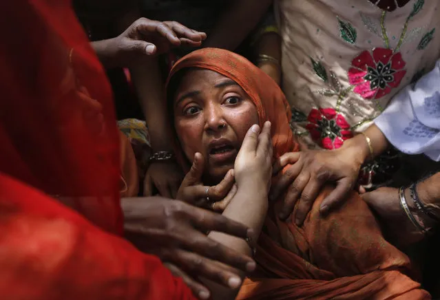 Local people console a shocked mother whose child was found under the debris of a residential building, in New Delhi, India, Wednesday, April 22, 2015. One man and a child were killed and at least nine others were injured when a three-storey residential building collapsed following an explosion in a cooking gas cylinder, according to local news agency Press Trust of India. (Photo by Manish Swarup/AP Photo)