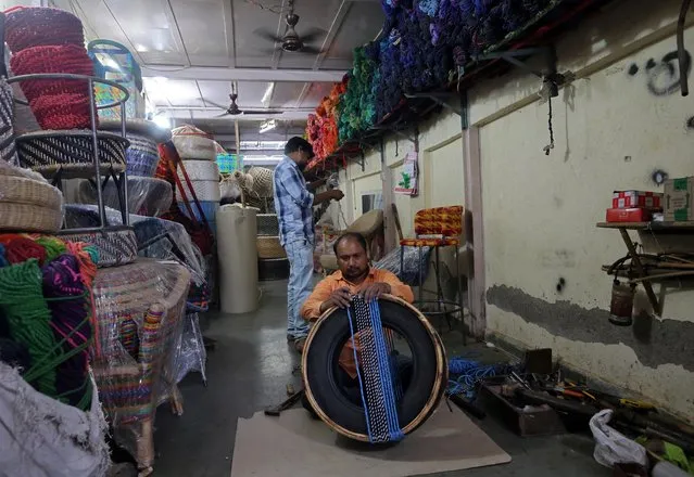 A man ties a rope made from garment waste around a used tyre to make a stool at a workshop in Mumbai, India, March 14, 2019. (Photo by Francis Mascarenhas/Reuters)