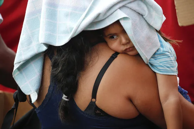 In this March 23, 2019 photo, a government supporter cradles a child as she listens to Venezuela's President Nicolas Maduro during an anti-imperialist rally in Caracas, Venezuela. Political turmoil in Venezuela increased when President Nicolas Maduro's 2018 re-election was deemed illegitimate by several governments and Assembly President Juan Guido declared himself interim president of the country. (Photo by Natacha Pisarenko/AP Photo)