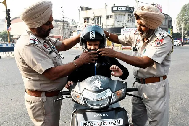 Police personnel distribute a helmet to a commuter to spread awareness on road safety measures and rules as Punjab is observing the “No Challan Day” where for one day police personnel do not issue any traffic offence fines, in Amritsar on November 14, 2021. (Photo by Narinder Nanu/AFP Photo)