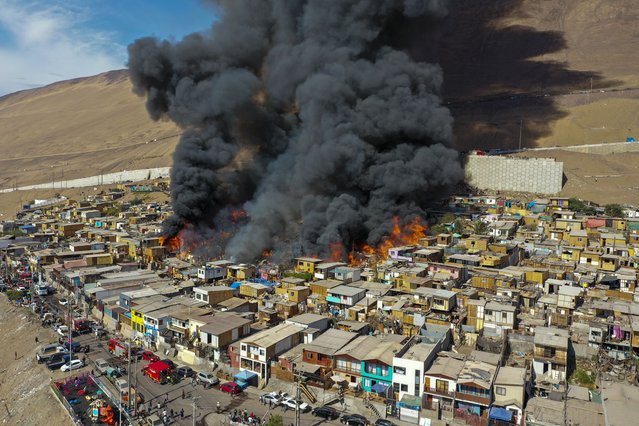 Houses burn during a fire in the low income neighborhood of Laguna Verde, in Iquique, Chile, Monday, January 10, 2022. According to authorities the fire destroyed close to 100 homes of the neighborhood which is populated mostly by migrants. (Photo by Ignacio Munoz/AP Photo)