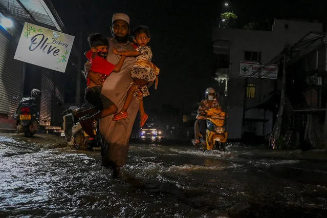 Residents wade through a flooded street after a heavy monsoon rainfall at Malwana, outside the capital Colombo on November 9, 2021. (Photo by Ishara S. Kodikara/AFP Photo)