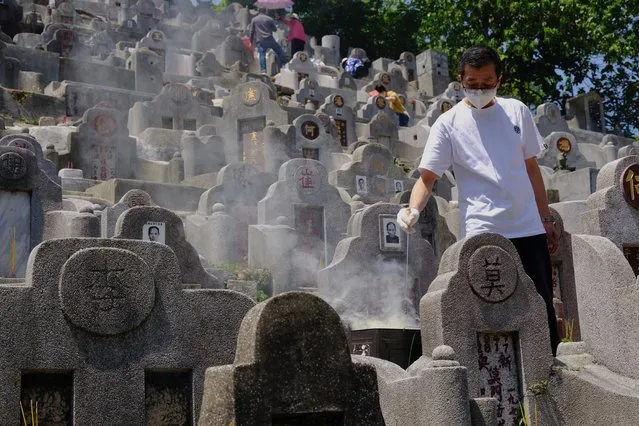 A man wearing face mask burns paper money at the gravesite of a relative in a cemetery during the Chinese Ching Ming, or Tomb Sweeping Day, in Hong Kong Tuesday, April 5, 2022. Thousands of Hong Kong residents pay respects to their ancestors and relatives during the annual festival. (Photo by Vincent Yu/AP Photo)