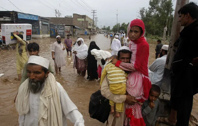 People make their way through a flooded street after heavy rains in a suburb of Peshawar, Pakistan, Thursday, July 23, 2015. The country's military has deployed helicopters and boats Wednesday to evacuate flood victims, as 285,000 have been affected by monsoon rains and flash floods in and around the city of Chitral in Pakistan's Khyber Pakhtunkhwa province, according to the National Disaster Management Authority. (Photo by Mohammad Sajjad/AP Photo)