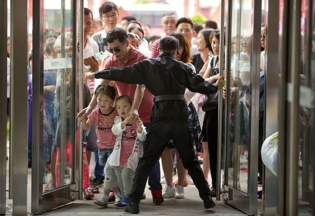 A security guard opens the entrance doors for the grand opening of the Wanda Mall at the Wanda Cultural Tourism City in Nanchang in southeastern China's Jiangxi province, Saturday, May 28, 2016. China's largest private property developer, the Wanda Group, opened an entertainment complex on Saturday that it's positioning as a distinctly homegrown rival to Disney and its $5.5 billion Shanghai theme park opening next month. (Photo by Mark Schiefelbein/AP Photo)