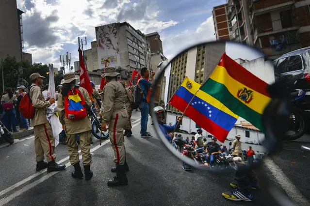 Reflected in a motorcycle side mirror, supporters of Venezuelan President Nicolas Maduro rally in support of former Bolivian President Evo Morales in Caracas, Venezuela, Monday, November 11, 2019. Morales stepped down following weeks of massive protests. (Photo by Matias Delacroix/AP Photo)