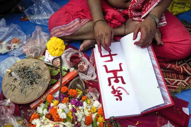 A Hindu priest marks a trader's account book with holy symbols on Bengali New Year's day in Kolkata, India, Friday, April 15, 2022. Traders in West Bengal open their new account books for the year on Bengali New Year after offering prayers to Lakshmi and Ganesha to bring them prosperity. (Photo by Bikas Das/AP Photo)