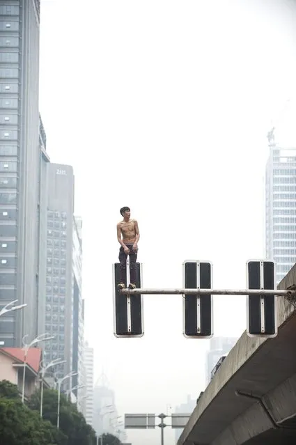 A topless man stands on top of a set of traffic signals as he threatens to jump on May 24, 2016 in Changsha, China. Police officers, fire workers and traffic police set up an inflatable safety cushion, but he missed it when he fell after trying to jump onto the overpass. An ambulance hurried the man to nearby hospital. (Photo by VCG via Getty Images)