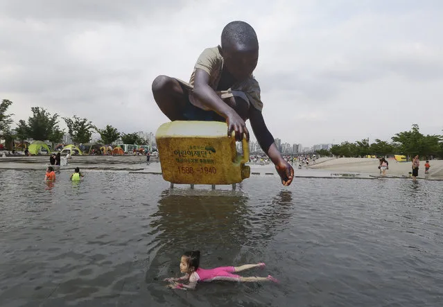 A girl swims to escape a heat in front of a large cutout that raises awareness on water shortage, at the Han River Park in Seoul, South Korea, Tuesday, August 4, 2015. A heat wave warning was issued in Seoul as temperatures soared above 32 degrees Celsius (89.6 Farenheit). (Photo by Ahn Young-joon/AP Photo)