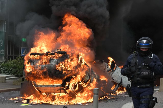 A police officer walks past a burning car at the end of a commemoration march for a teenage driver shot dead by a policeman, in the Parisian suburb of Nanterre, on June 29, 2023. Violent protests broke out in France in the early hours of June 29, 2023, as anger grows over the police killing of a teenager, with security forces arresting 150 people in the chaos that saw balaclava-clad protesters burning cars and setting off fireworks. Nahel M., 17, was shot in the chest at point-blank range in Nanterre in the morning of June 27, 2023, in an incident that has reignited debate in France about police tactics long criticised by rights groups over the treatment of people in low-income suburbs, particularly ethnic minorities. (Photo by Alain Jocard/AFP Photo)