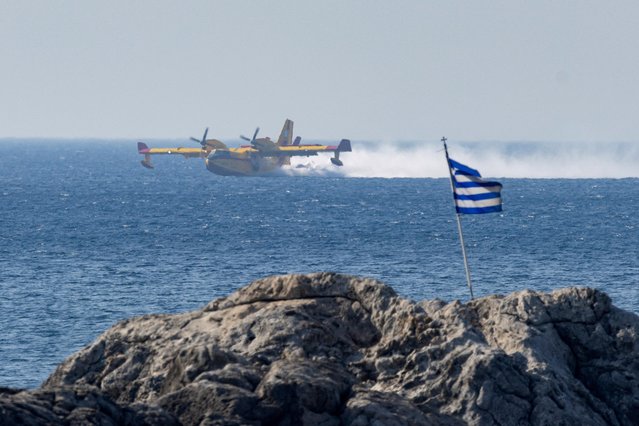 A firefighting plane is seen, as a Greek national flag flutters, near the village of Gennadi, on the island of Rhodes, Greece on July 24, 2023. (Photo by Nicolas Economou/Reuters)