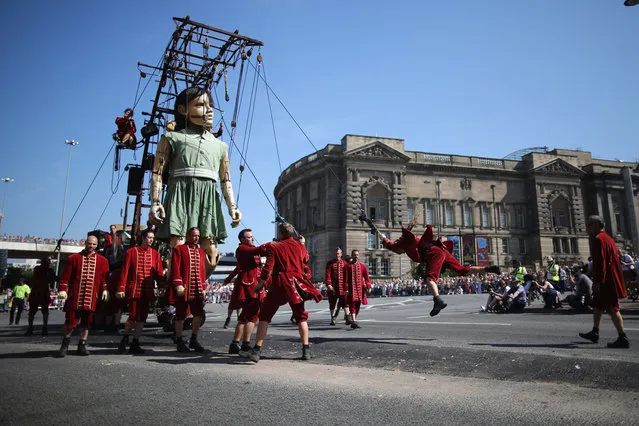 A puppeteer swings on a rope as the Little Giant Girl walks through the streets of Liverpool on July 25, 2014 in Liverpool, England. French street theatre company Royal de Luxe are putting on a show throughout the city as part of Liverpool's World War I centenary commemorations from July 23-27. The giant puppet grandmother has slept in the hall for two days as part of “Memories of August 1914”. (Photo by Christopher Furlong/Getty Images)