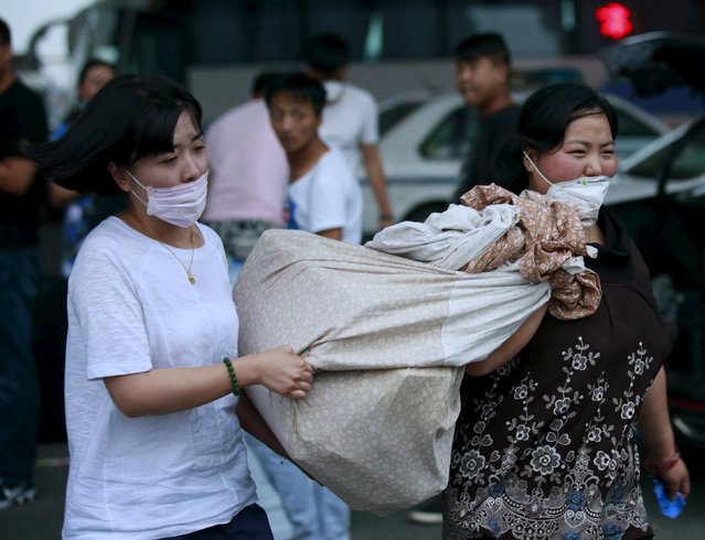 Evacuated residents who went back to their homes to collect belongings, carry a bundle on a road near the evacuated residential area at Binhai new district in Tianjin, China, August 17, 2015. (Photo by Kim Kyung-Hoon/Reuters)