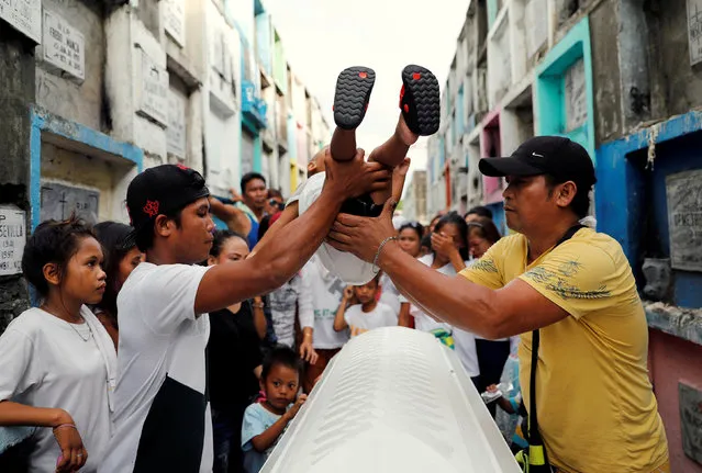 Relatives carry a child over the coffin as a Filipino custom to let the spirit of the departed rest, in Navotas city, Metro Manila, Philippines August 27, 2017. (Photo by Dondi Tawatao/Reuters)