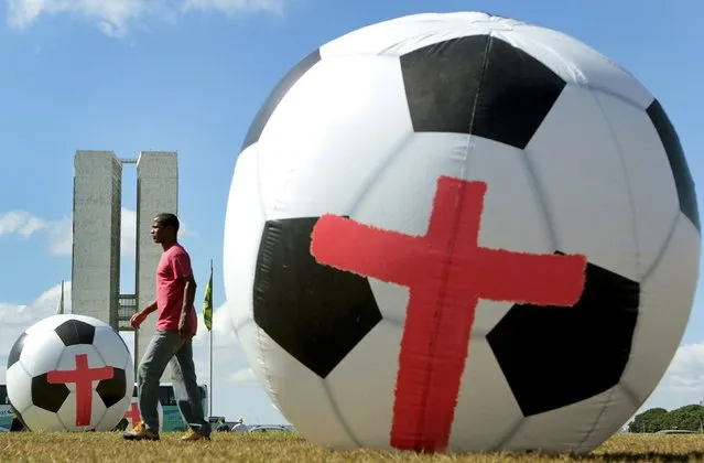 A man walks between giant inflatable soccer balls marked with red crosses placed by members of non-governmental organization (NGO) Rio de Paz (Rio Peace) during a protest in front of the National Congress in Brasilia June 3, 2014. (Photo by Joedson Alves/Reuters)