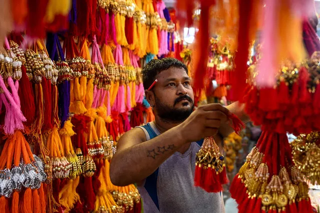 A shopkeeper arranges his display of Rakhis which a sacred thread used in the Hindu festival of Raksha Bandhan, at a shop in the walled city part of New Delhi on August 6, 2022. (Photo by Sajjad Hussain/AFP Photo)