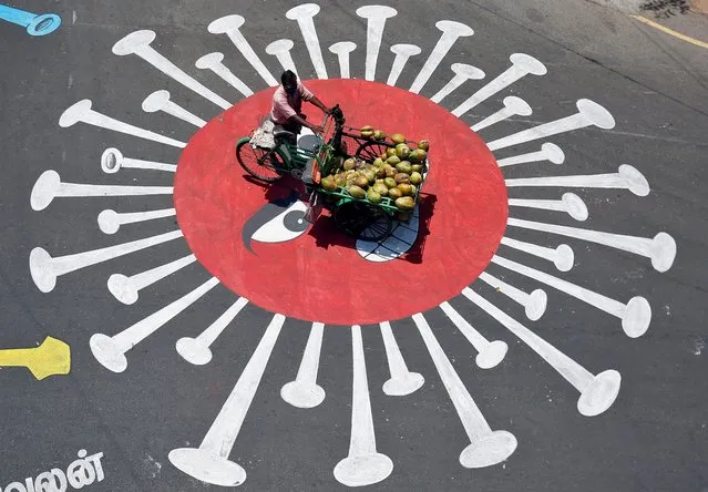 A man selling coconuts rides his trishaw on a graffiti on a road depicting the coronavirus as an attempt to raise awareness about the importance of staying at home during a 21-day nationwide lockdown to slow the spreading of the coronavirus disease (COVID-19), in Chennai, India, April 13, 2020. (Photo by P. Ravikumar/Reuters)
