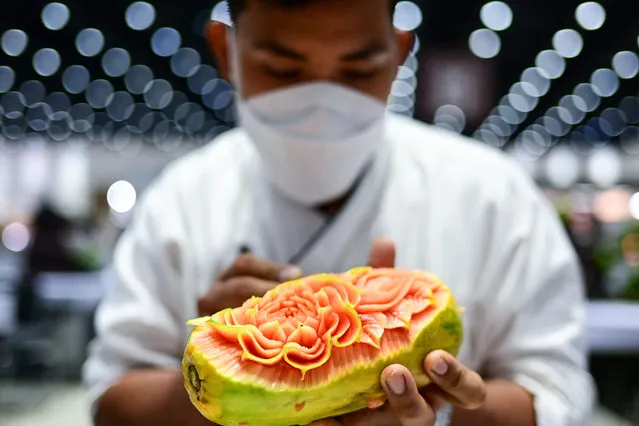 A Thai participant carves patterns into a papaya during a fruit and vegetable carving competition at the 26th Thailand International Culinary Cup in Bangkok on September 21, 2022. (Photo by Manan Vatsyayana/AFP Photo)
