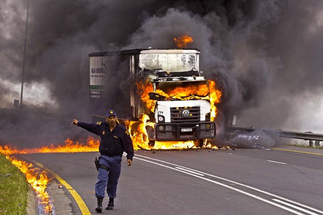 A police man keeps traffic away from a burning truck after it was set ablaze by striking truck drivers, on a main highway leading out of Cape Town, South Africa, on October 3, 2012. The drivers have been on strike for the past two weeks. (Photo by Schalk van Zuydam/Associated Press)
