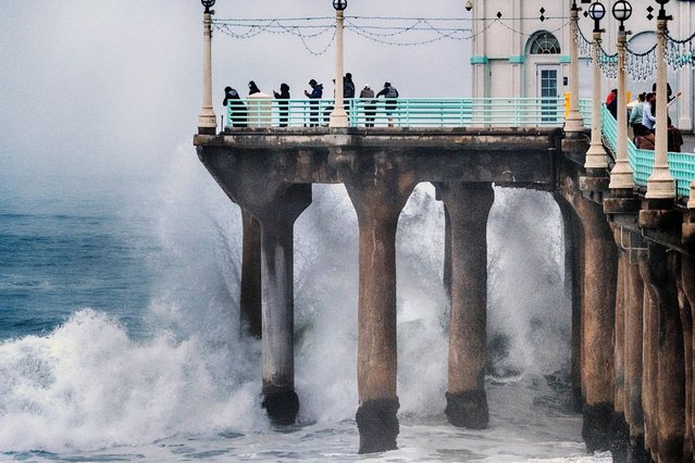 People stand at the end of the Manhattan Beach Pier and watch high surf pound the pylons on Tuesday, December 24, 2024 in Manhattan Beach, Calif. (Photo by Richard Vogel/AP Photo)