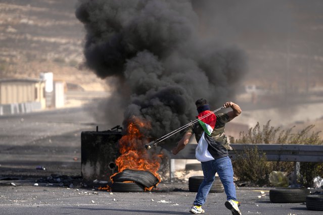 A Palestinian protester uses a slingshot during clashes with Israeli army troops in the West Bank city of Ramallah, Thursday, October 20, 2022. Palestinians launched a general strike on Thursday throughout the West Bank and east Jerusalem in response to the death of a suspected Palestinian attacker. (Photo by Nasser Nasser/AP Photo)