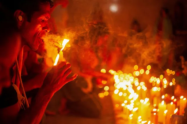 A man lights a cigar at the “Altar Mayor”, a place of prayer and to where people bring candles and flowers for the saints, during the annual religious festival revering the goddess Maria Lionza, in Quibayo, Venezuela on October 11, 2022. (Photo by Nica Guerrero/Reuters)