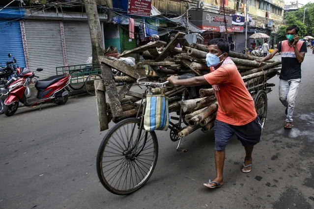 People wearing masks as a precaution against the coronavirus transport scrap on a rickshaw in Kolkata, India, Tuesday, July 21, 2020. (Photo by Bikas Das/AP Photo)