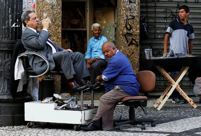 A customer drinks a bottle of water as his shoes are polished by a shoe shiner on a street in downtown Sao Paulo, Brazil on April 8, 2014. (Photo by Nacho Doce/Reuters)