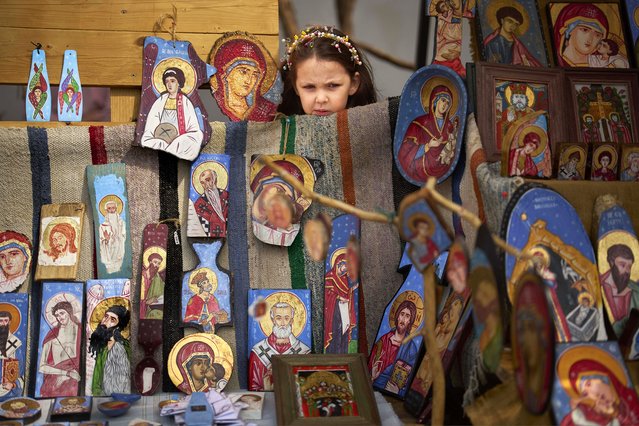 A child peers from behind a stand of an artist selling religious icons at a fair in Bucharest, Romania, April 5, 2025. (Photo by Vadim Ghirda/AP Photo)
