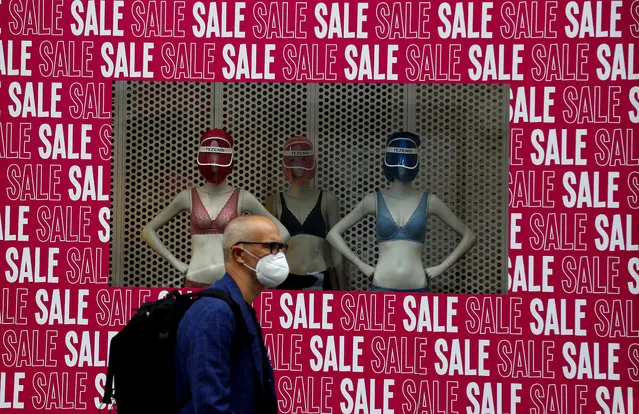 A man wearing a protective face mask walks past a shop window in London, Tuesday, July 14, 2020. Britain's government is demanding people wear face coverings in shops as it has sought to clarify its message after weeks of prevarication amid the COVID-19 pandemic. (Photo by Frank Augstein/AP Photo)